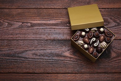 Open box of delicious chocolate candies on wooden table, top view. Space for text