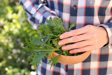 Photo of Woman holding wooden bowl with fresh mizuna leaves outdoors, closeup
