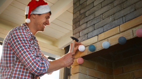 Man in Santa hat decorating fireplace in house with Christmas lights