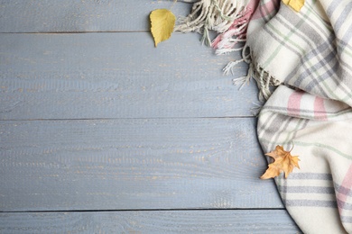 Photo of Checkered plaid and dry leaves on light grey wooden table, flat lay. Space for text