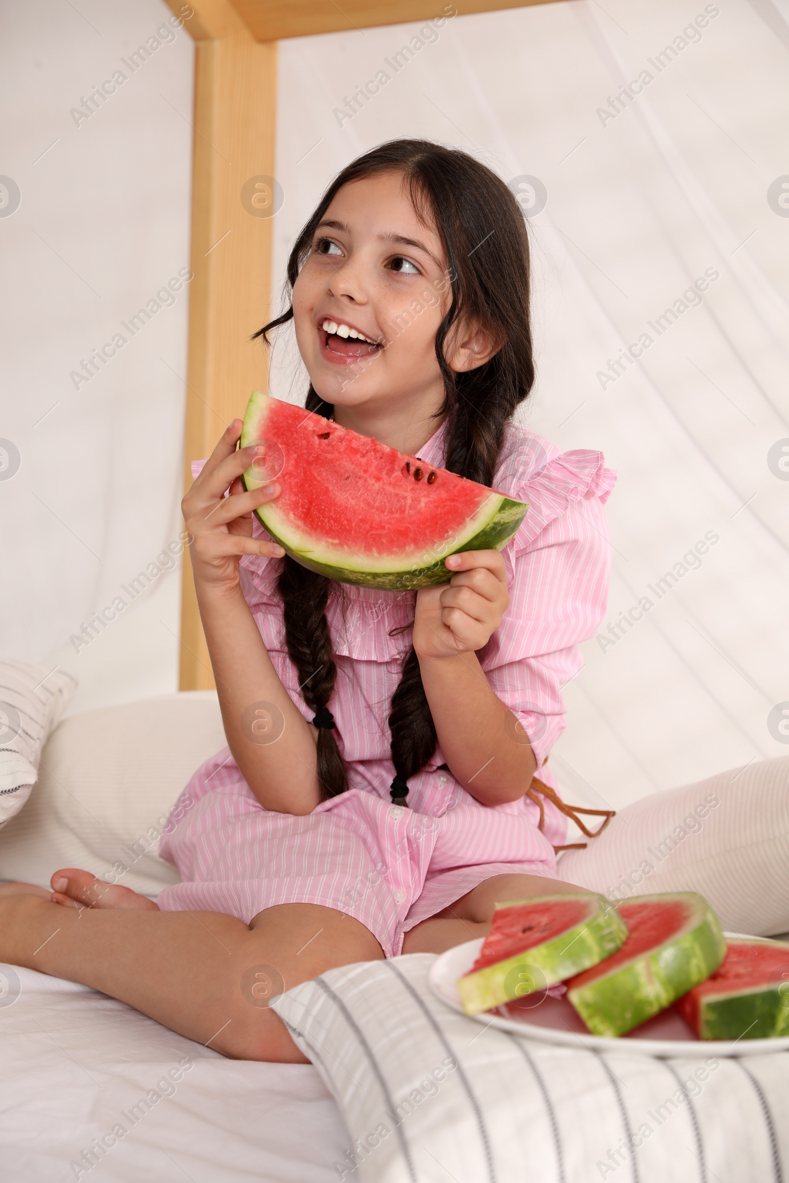 Photo of Cute little girl with watermelon on bed at home