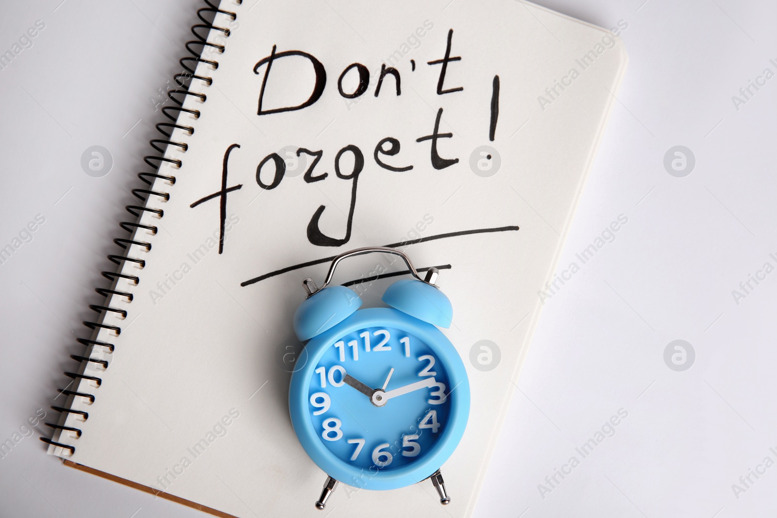 Photo of Alarm clock and notebook with text Don't forget on light grey background, top view. Reminder concept