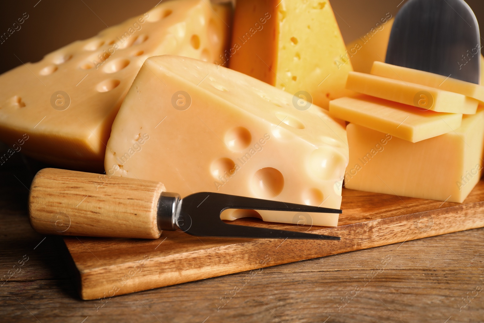 Photo of Different sorts of cheese, fork and knife on wooden table, closeup