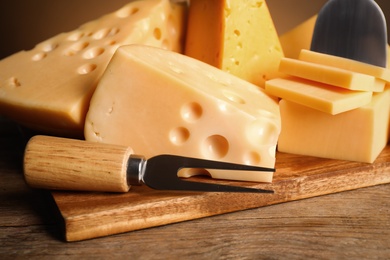 Photo of Different sorts of cheese, fork and knife on wooden table, closeup