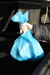 Photo of Woman throwing trash bag full of garbage in bin outdoors, closeup