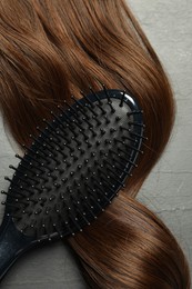 Photo of Stylish brush with brown hair strand on dark grey table, top view