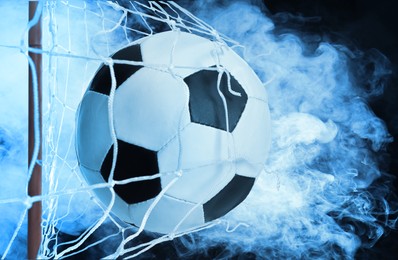 Soccer ball in net and white smoke against black background