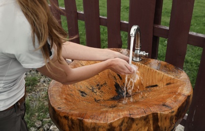 Photo of Woman washing hands under tap outdoors, closeup
