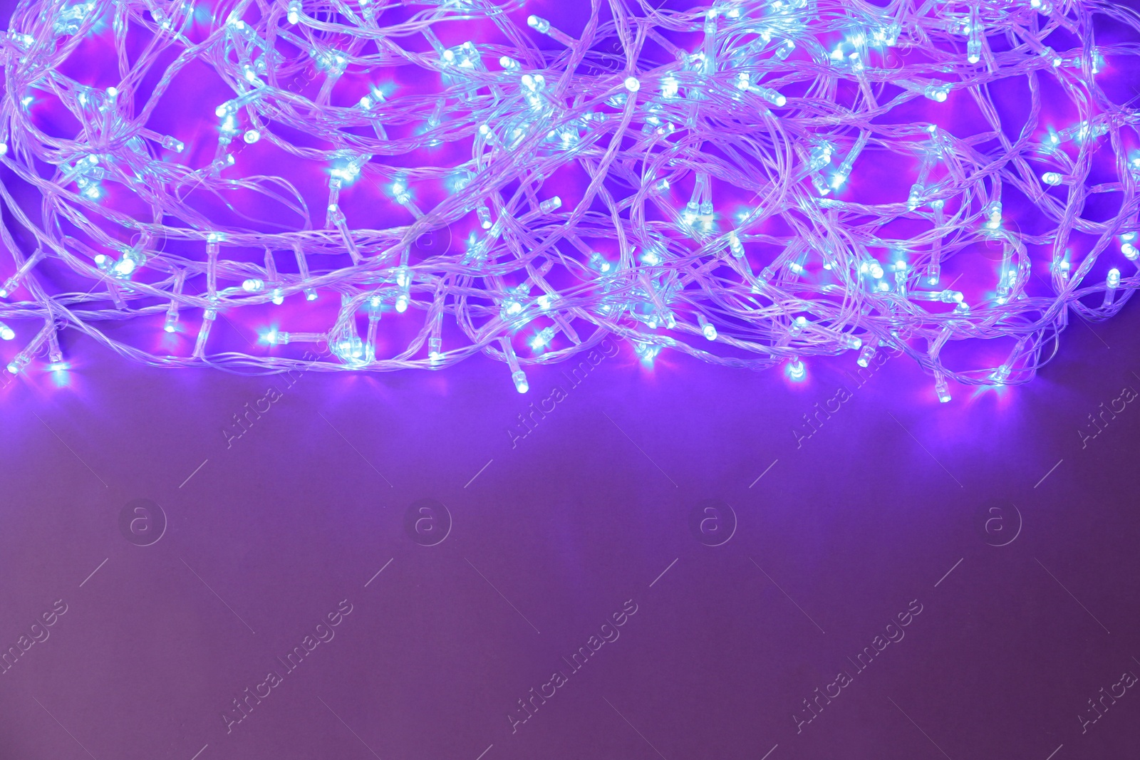 Photo of Glowing Christmas lights on violet background, top view. Space for text