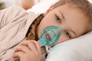 Photo of Little girl using nebulizer for inhalation on bed indoors, closeup