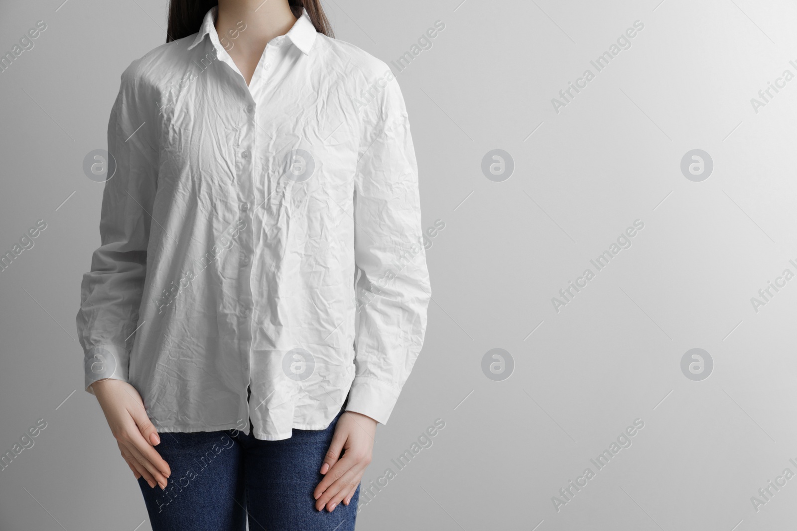 Photo of Woman wearing wrinkled white blouse on light grey background, closeup. Space for text