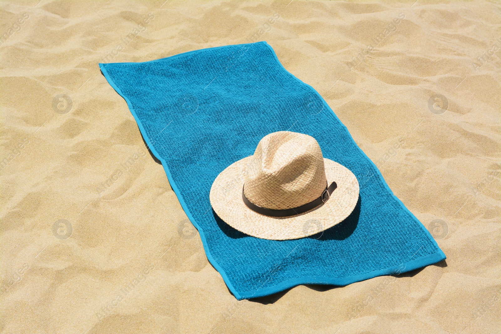 Photo of Soft blue towel and straw hat on sandy beach