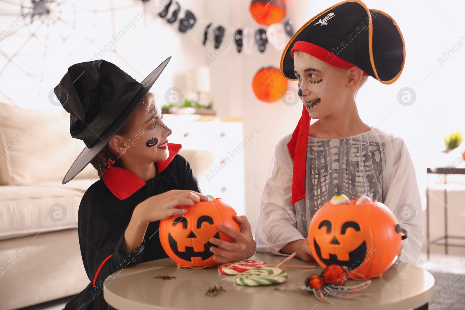 Photo of Cute little kids with pumpkin candy buckets wearing Halloween costumes at home