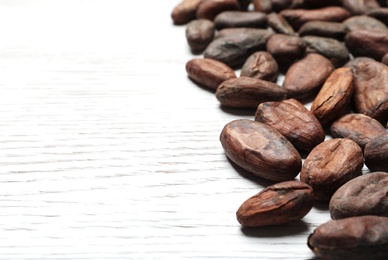 Tasty cocoa beans on white wooden table, space for text