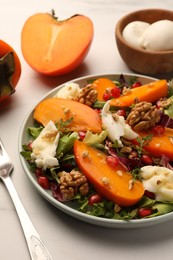 Photo of Delicious persimmon salad with cheese and pomegranate served on white table, closeup