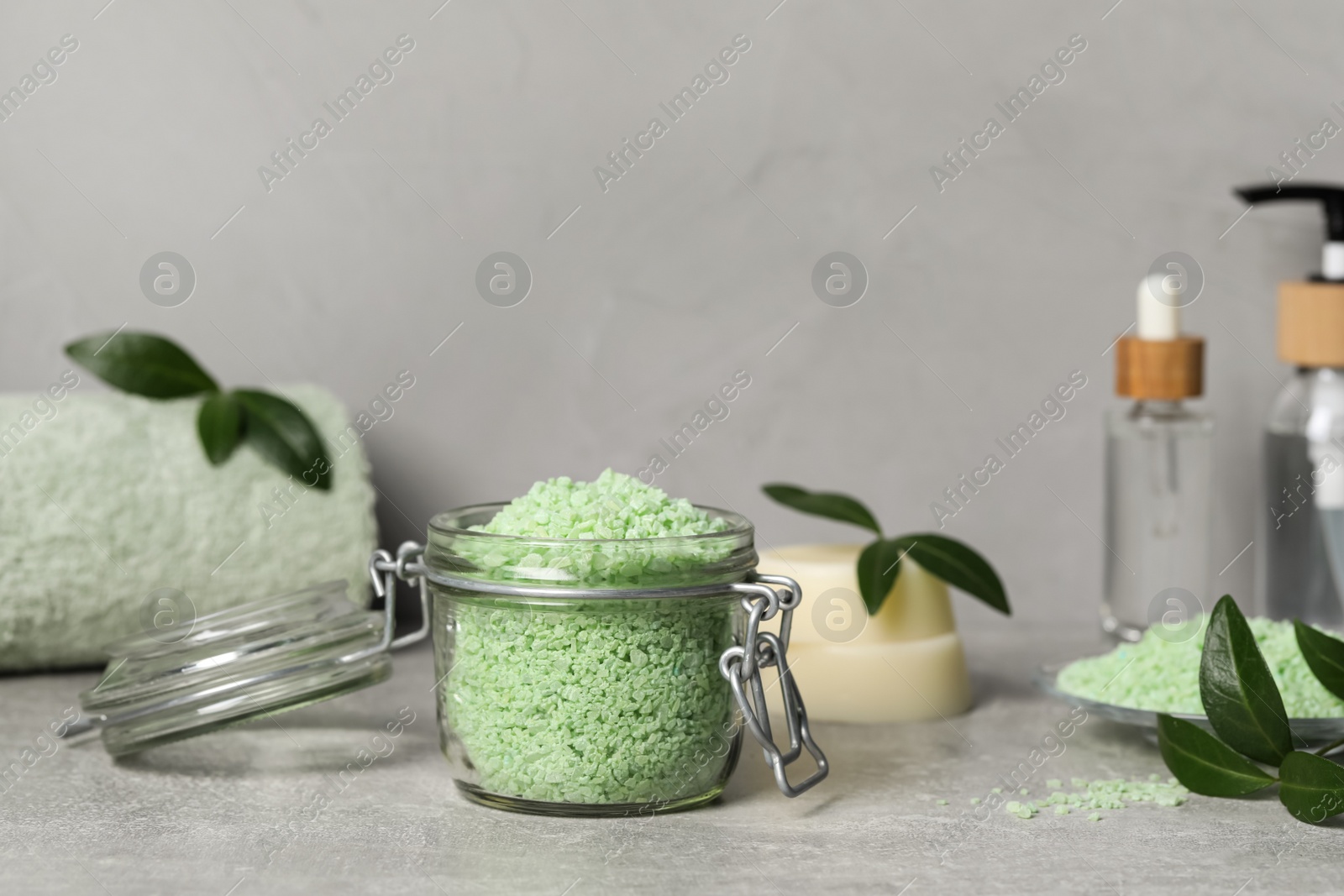 Photo of Jar with natural sea salt, green leaves and cosmetic products on light grey table