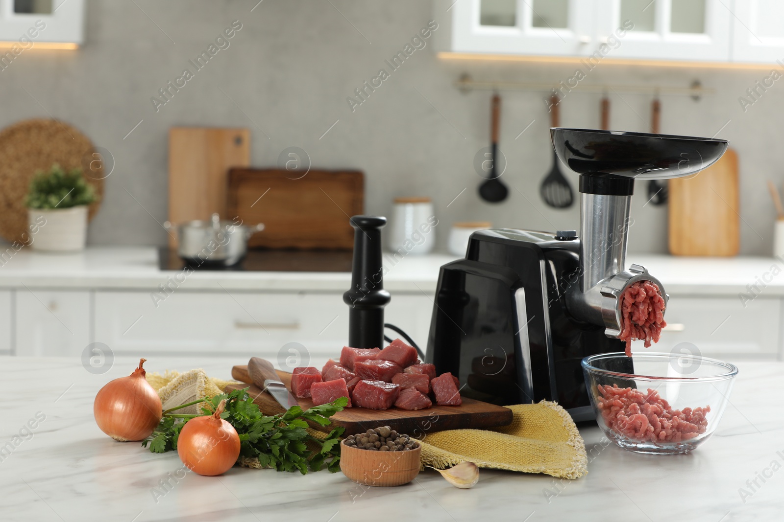 Photo of Electric meat grinder with beef mince and products on white table in kitchen