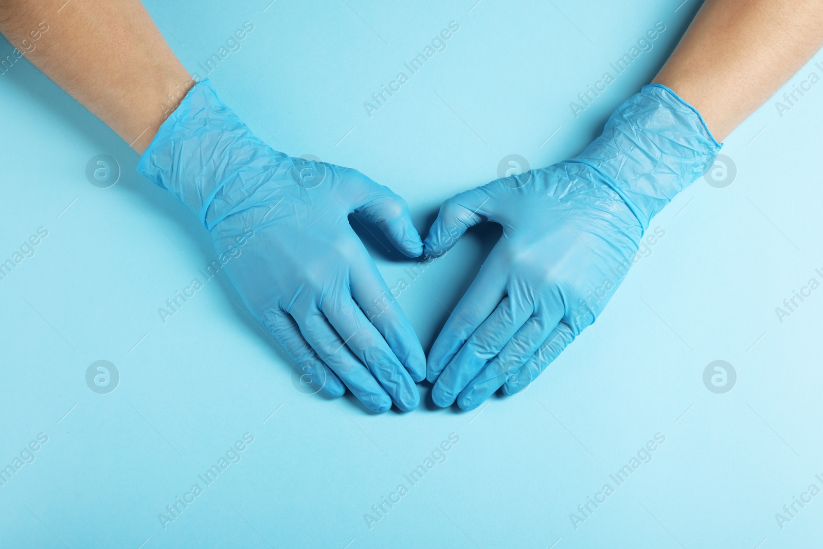 Photo of Doctor wearing medical gloves making heart gesture on light blue background, top view