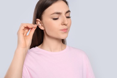 Young woman cleaning ear with cotton swab on light grey background