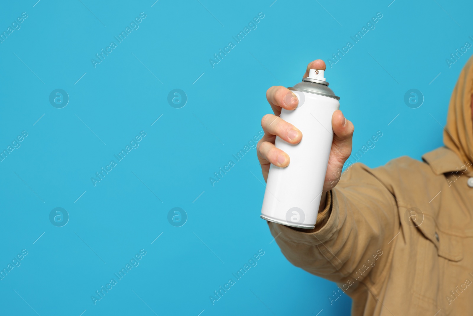 Photo of Man holding white can of spray paint on light blue background, closeup. Space for text