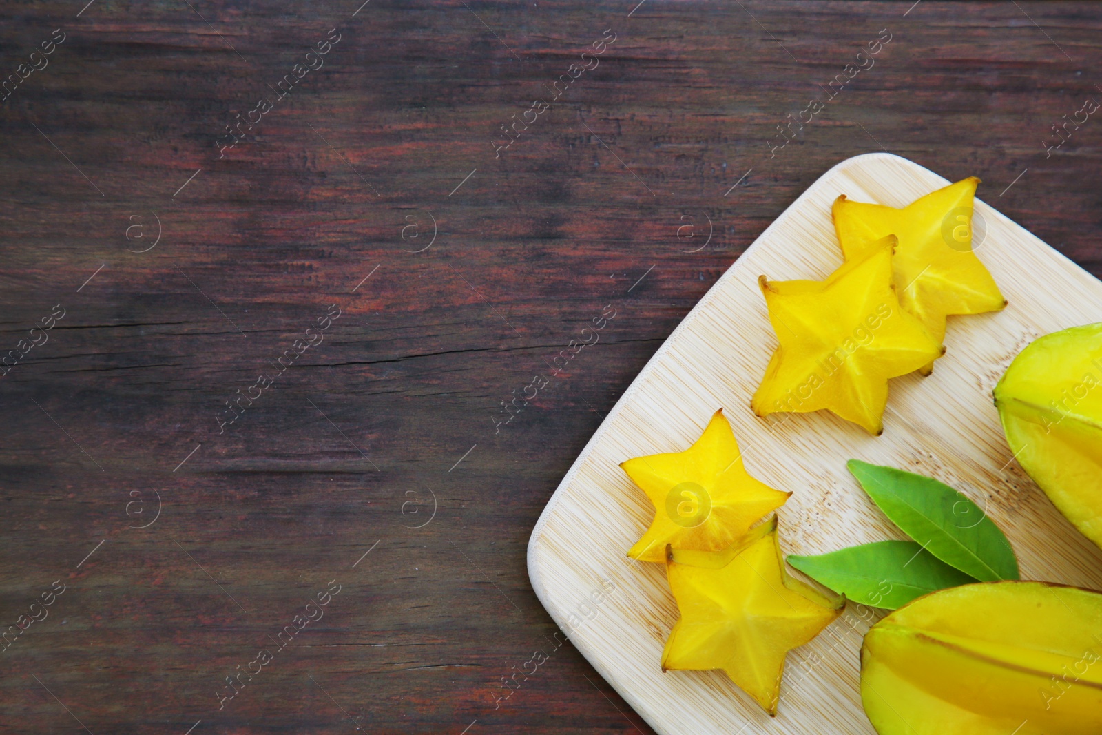 Photo of Delicious cut and whole carambolas with green leaves on wooden table, top view. Space for text