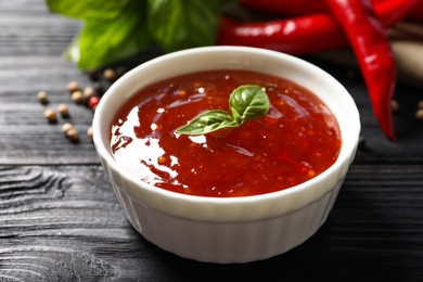 Photo of Spicy chili sauce with basil on dark wooden table