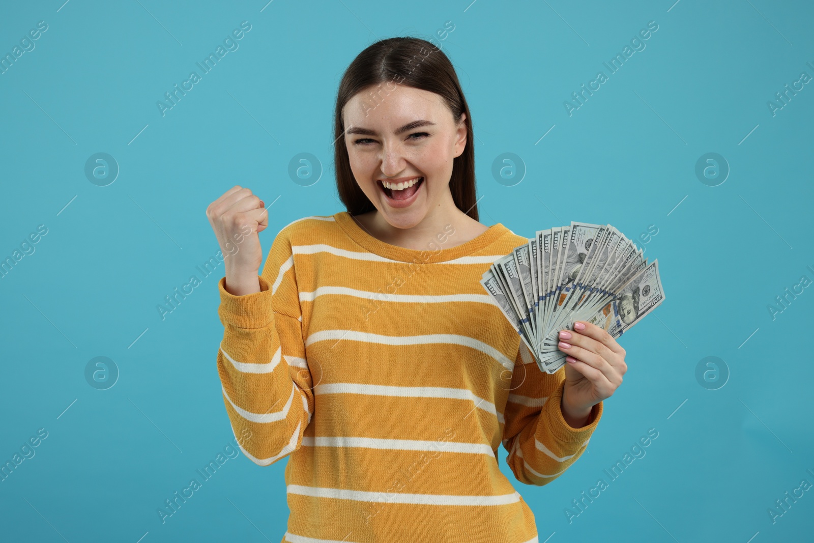 Photo of Excited woman with dollar banknotes on light blue background