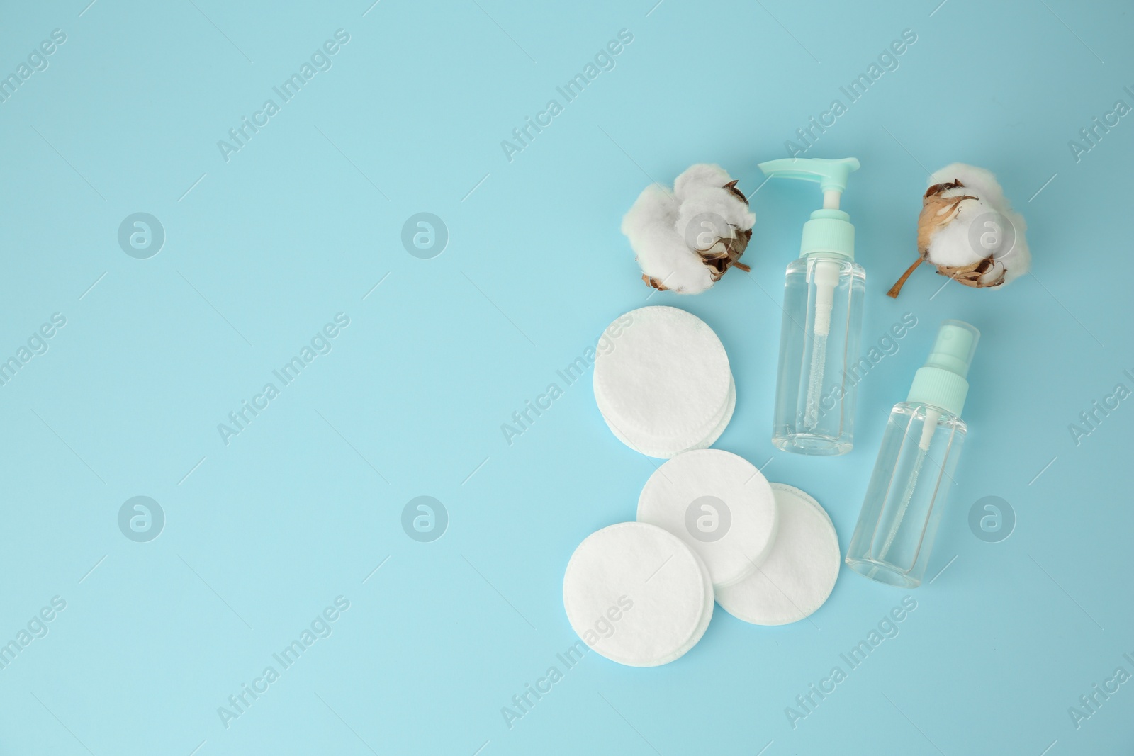 Photo of Cosmetic products, cotton pads and flowers on light blue background, flat lay. Space for text