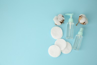 Photo of Cosmetic products, cotton pads and flowers on light blue background, flat lay. Space for text