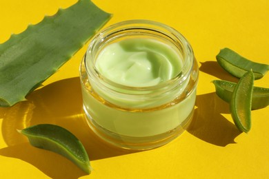 Jar with cream and cut aloe leaves on yellow background, closeup