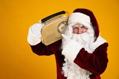 Photo of Santa Claus with vintage radio on yellow background. Christmas music