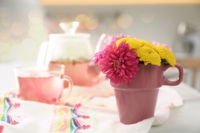 Photo of Beautiful bright flowers in pink cup, fabric and aromatic tea on table indoors, space for text