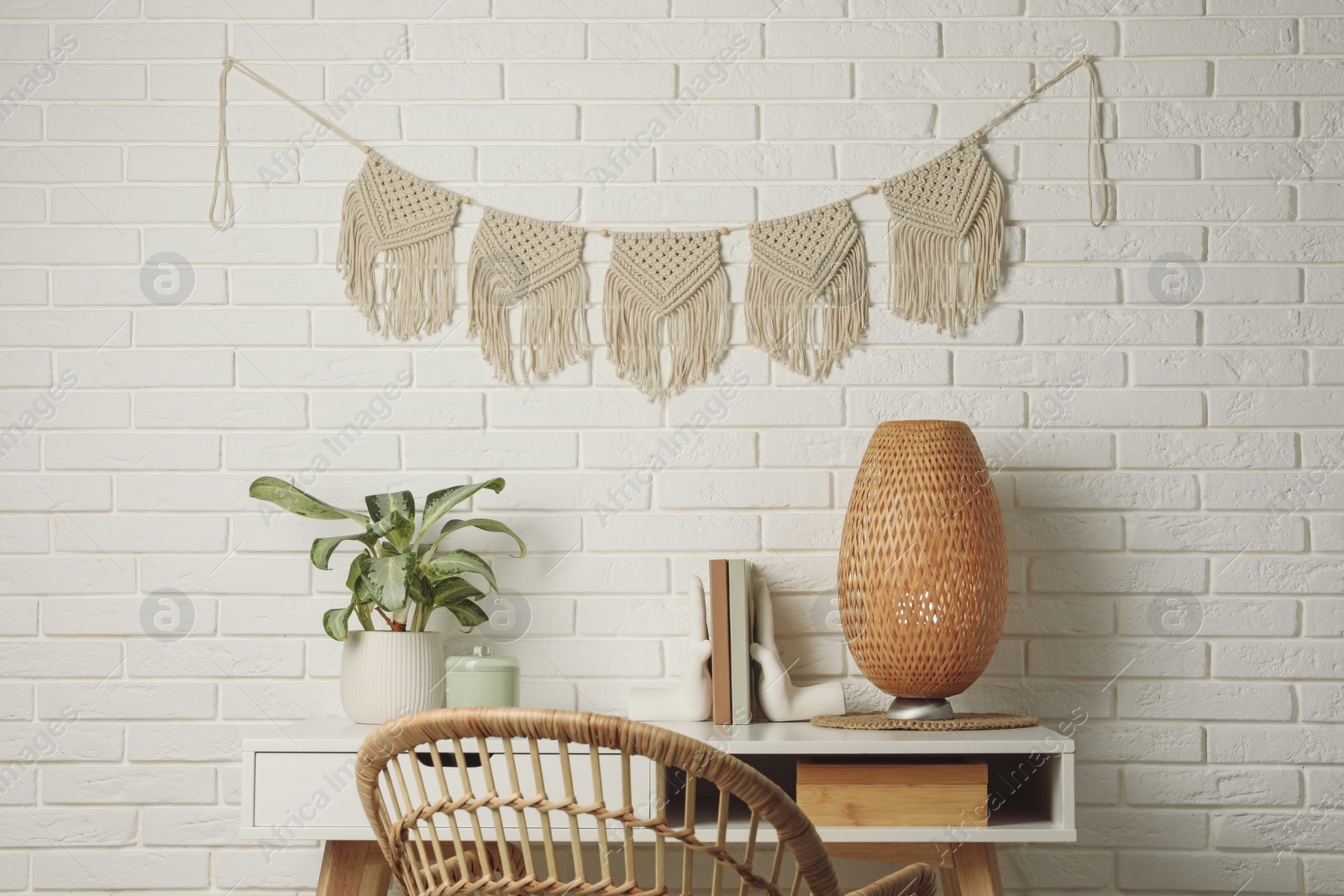 Photo of Potted houseplant, decor elements and books on white table near brick wall with stylish macrame