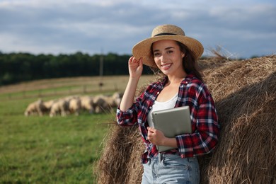 Farmer with tablet near hay bale on farm. Space for text