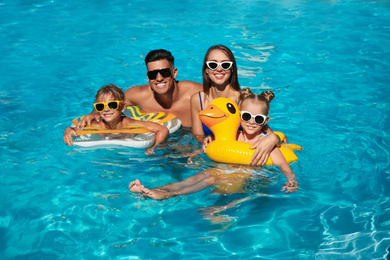 Photo of Happy family with inflatable rings in outdoor swimming pool on sunny summer day