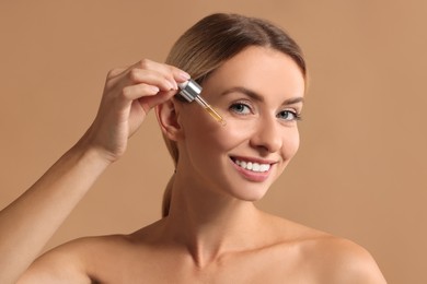 Photo of Beautiful woman applying cosmetic serum onto her face on beige background
