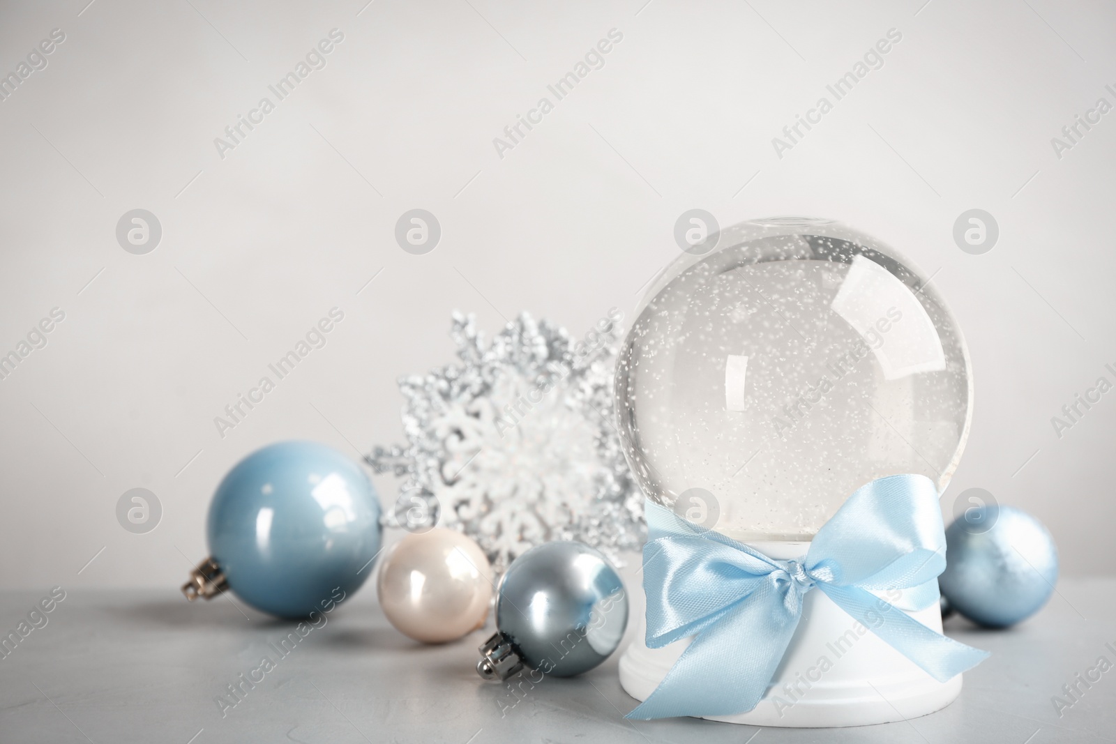 Photo of Beautiful snow globe and Christmas decor on light grey stone table, space for text