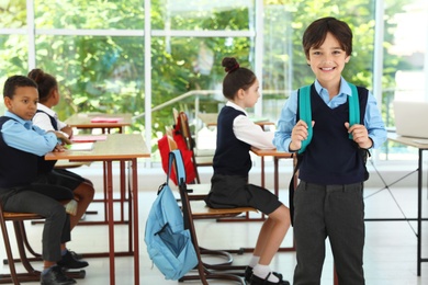 Boy wearing school uniform with backpack in classroom