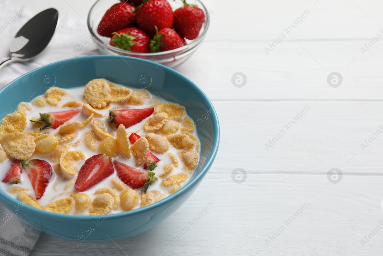 Photo of Bowl of tasty crispy corn flakes with milk and strawberries on white wooden table. Space for text