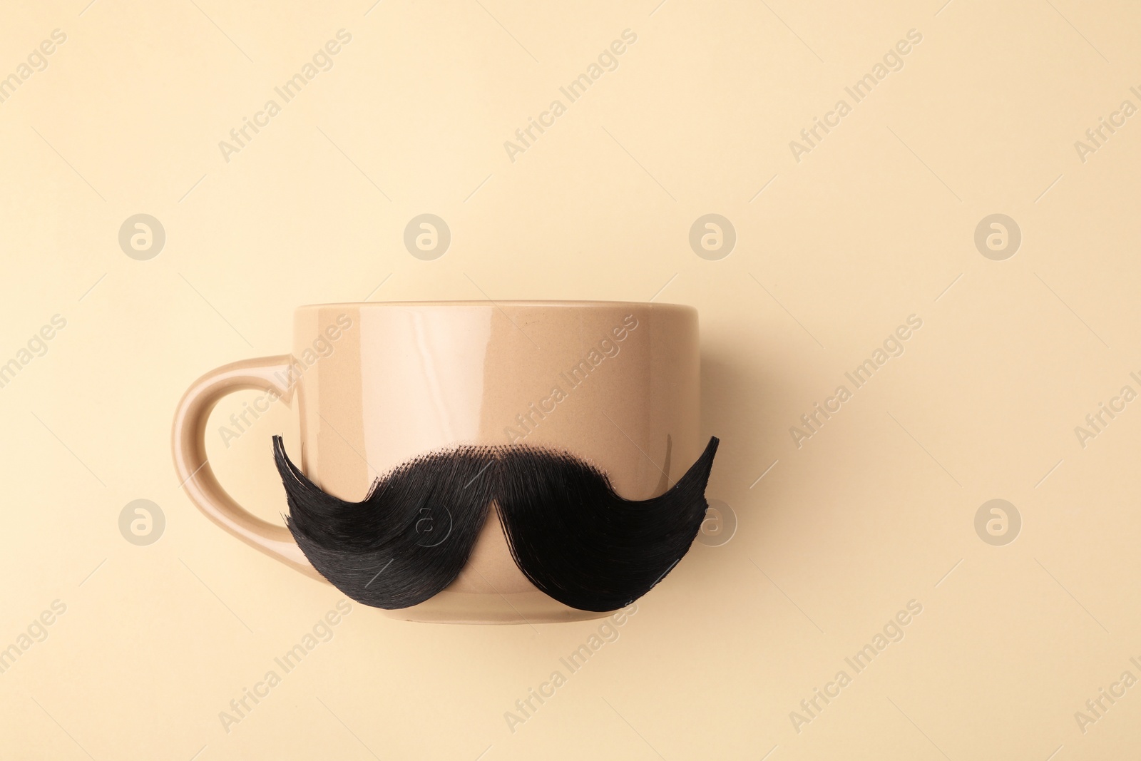 Photo of Artificial moustache and cup on beige background, top view. Space for text