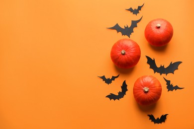 Photo of Flat lay composition with pumpkins and paper bats on orange background, space for text. Halloween decor