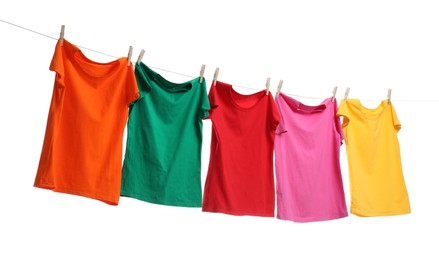 Photo of Different bright t-shirts drying on washing line against white background