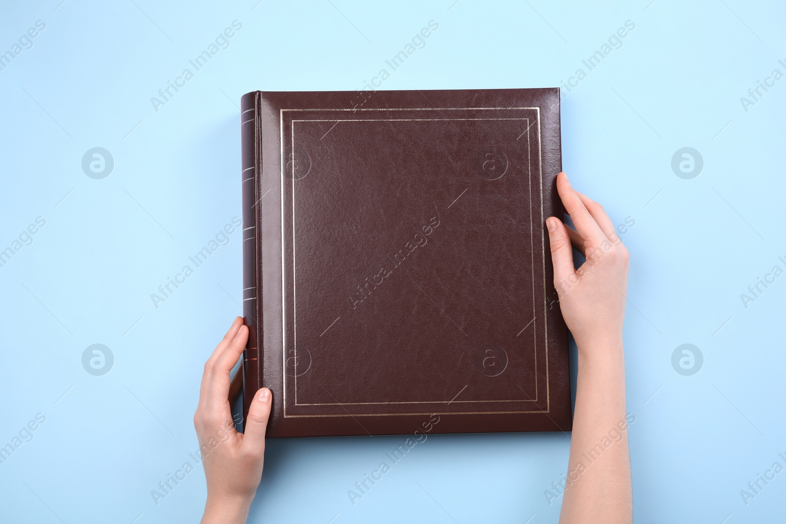 Photo of Woman with photo album at light blue background, top view