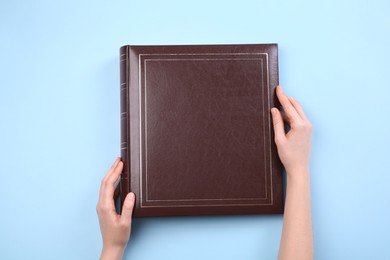 Photo of Woman with photo album at light blue background, top view