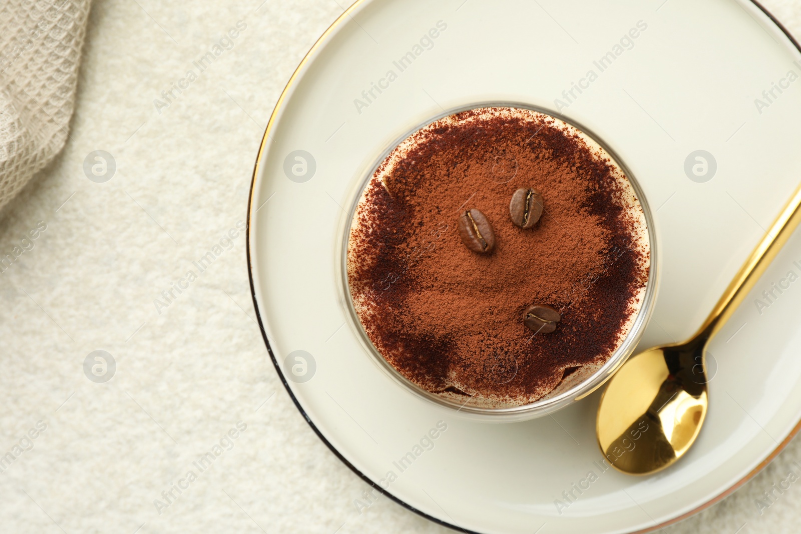 Photo of Delicious tiramisu in glass, coffee beans and spoon on white table, top view. Space for text