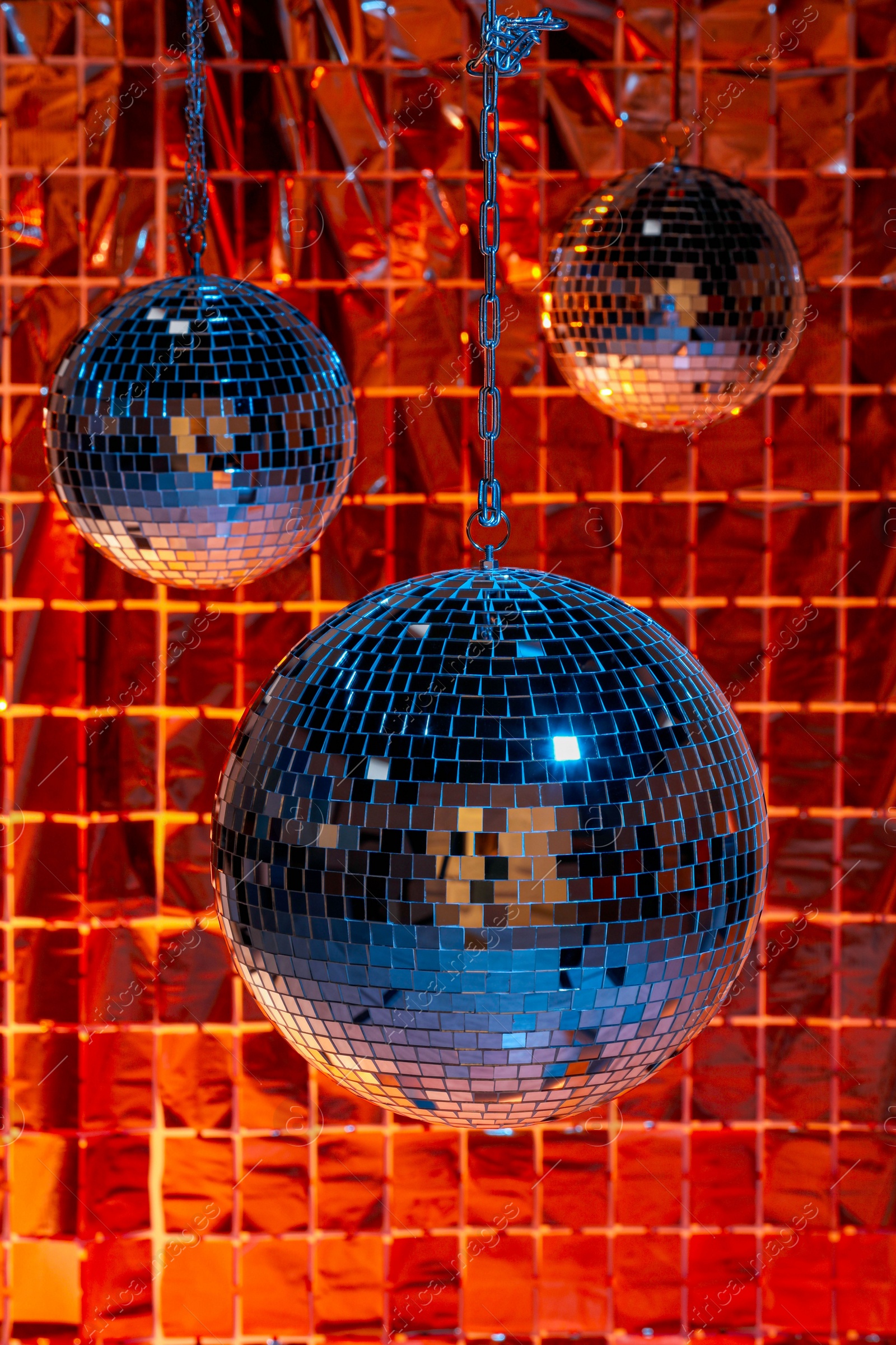 Photo of Shiny disco balls against foil party curtain under color lights