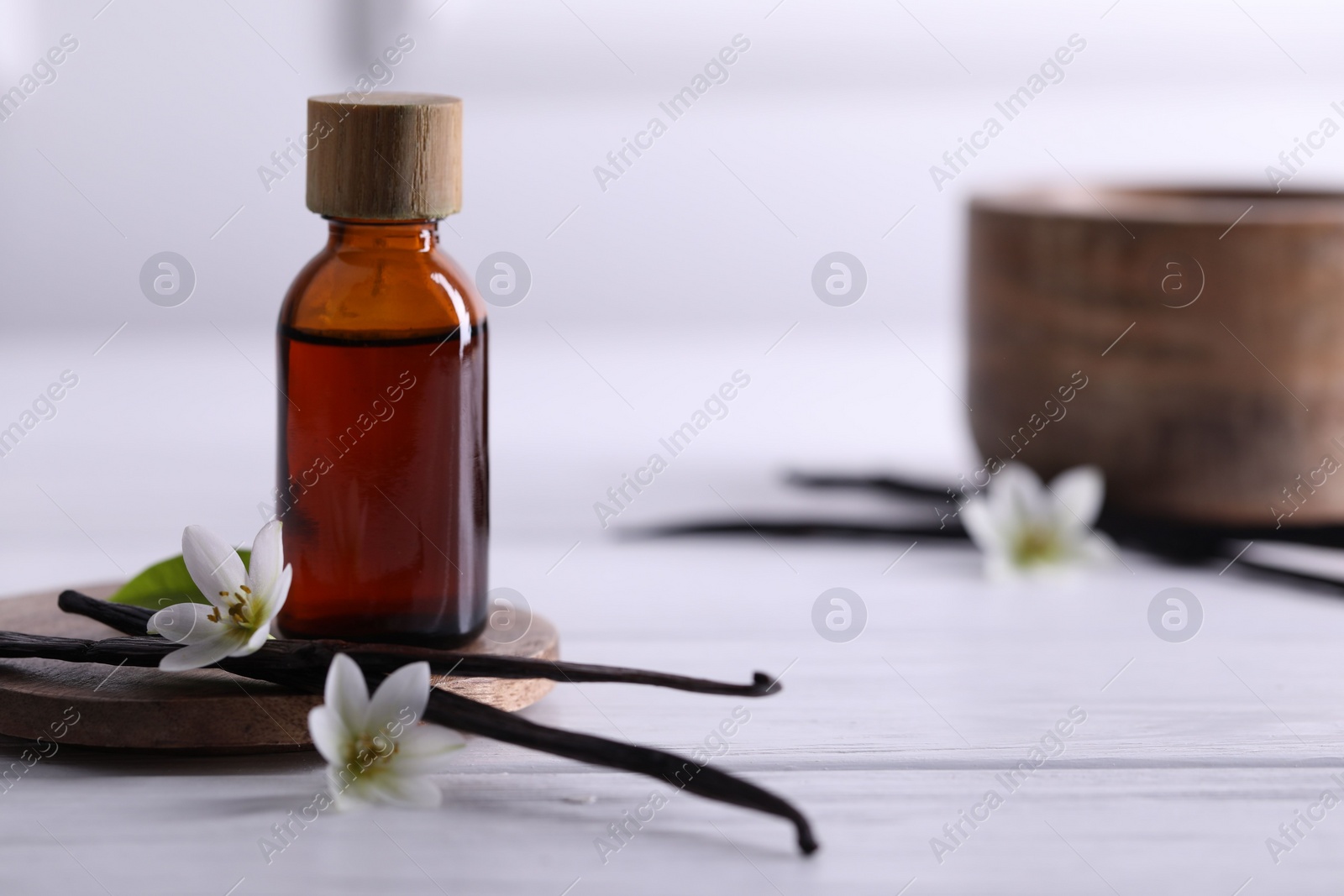 Photo of Vanilla pods, flowers and bottle with essential oil on white wooden table, closeup