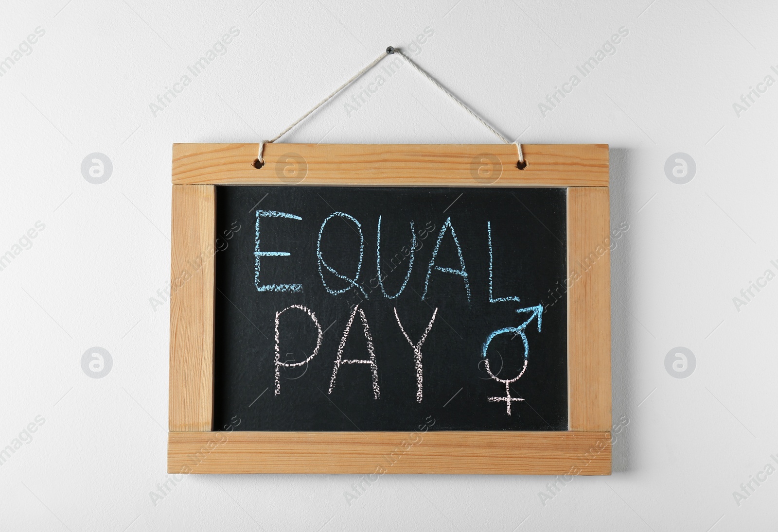 Photo of Blackboard with words Equal Pay and gender symbols hanging on white wall