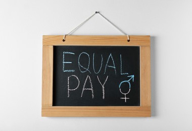 Photo of Blackboard with words Equal Pay and gender symbols hanging on white wall