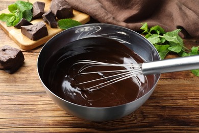 Photo of Delicious chocolate cream and whisk in bowl on wooden table, closeup